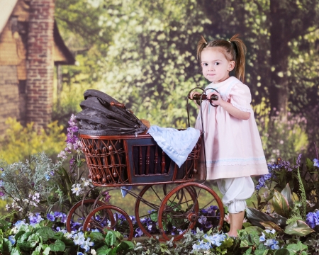 A beautiful preschooler pushing an antique doll buggy in a rustic, rural setting.  の写真素材