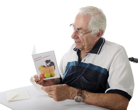 Closeup image of an elderly man reading a get well card while sitting in his wheelchair.  On a white background.の写真素材