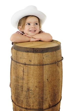 An adorable preschool cowgirl resting her head on a rustic wood barrel.  On a white background with space for your text on the barrel.  の写真素材