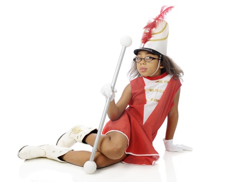 An elementary drum majorette sitting on the ground with her baton.  On a white background.