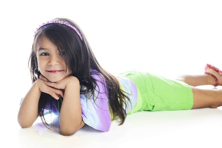 A beautiful young elementary girl looking at the viewer while laying on her belly in casual summer...
