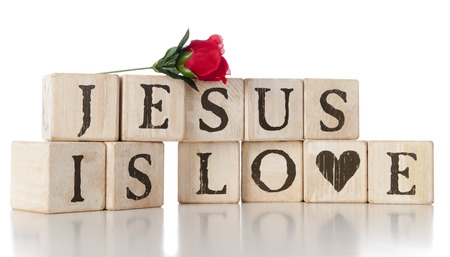 Two layers of rustic alphabet blocks spelling out "Jesus is Love."  A red rose rests on top. On a white background.の写真素材