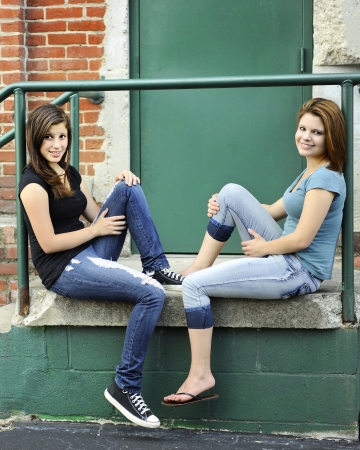 Two young teen girls relaxing together on an old warehouse stoop. の写真素材