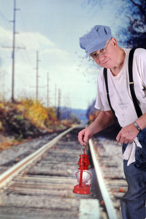 A senior train engineer signalling "train coming" with his red langern.  の写真素材