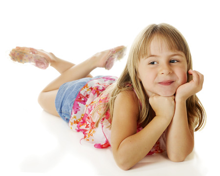 A pretty, young elementary girl happily relaxed on the floor with her head supported by her hands.  On a white background.の写真素材