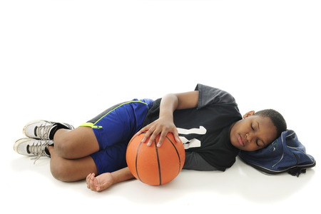 A preteen athlete asleep with his head on his gym bag and hand resting on his basketball.  On a white background with space over the sleeper for your text.の写真素材