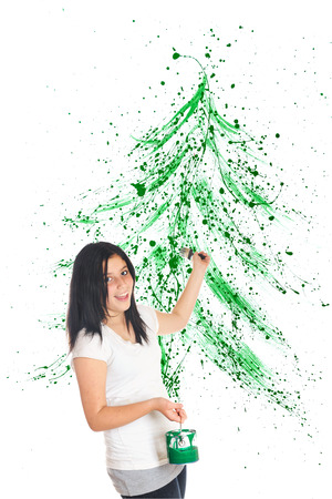 An attractive preteen flinging green paint to create a splattered Christmas tree image behind her.  On a white background.の写真素材