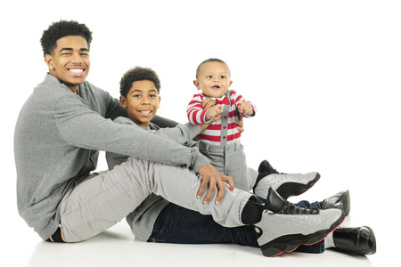 Three widely-spaced brothers sitting train-style from the tall teen oldest to the infant youngest.  On a white background.の写真素材