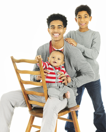 A portrait of three widely-spaced brothers -- the oldest sitting on a chair backwards while holding...