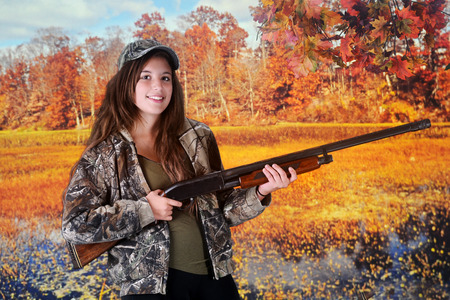 A beautiful young hunter smiling with her rifle among colorful fall foliage.