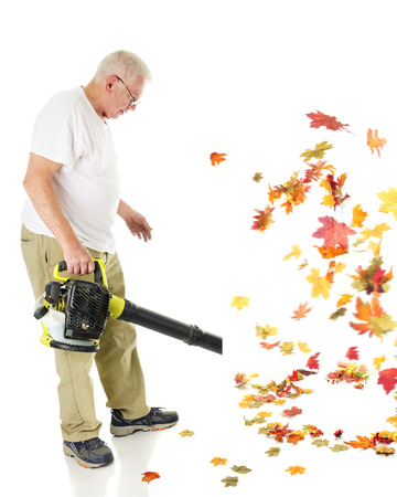A senior man blowing autumn leaves with his gas driven leaf blower.  Motion blur on leaves.  On a white background.の写真素材