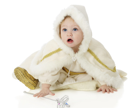 An adorable baby "snow princess" reaching for her wand while looking up questioningly.  On a white background.の写真素材