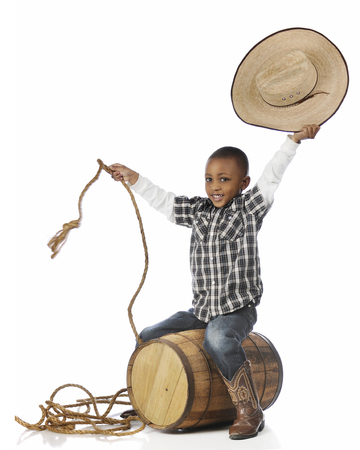 A happy young boy smiling at the viewer as he "ridies" an old barrel as he plays cowboy.  On a white background.の写真素材