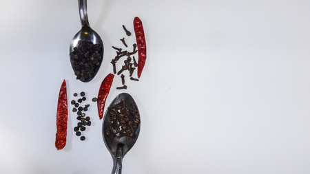 Chili clove and pepper arranged side by side on two spoons and white backgroundの写真素材