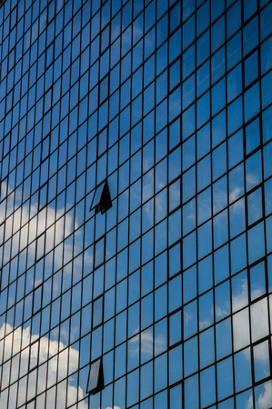 The sky and clouds are reflected in the glass of a skyscraper
