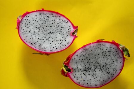 Fresh sliced dragonfruit or pitaya against a vibrant yellow background to show color contrast,...