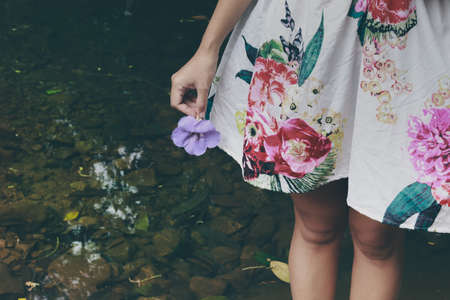 Low section of a woman in floral dress holding a flower showing the concept of Spring and Summerの写真素材