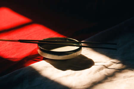 Light and shadows cast on a ceramic incense holder and sticks showing zen, wellness and mindfulnessの写真素材