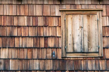 Weathered and faded from the sun wooden shingles that are the facade of an alpine house. Wooden texture in shades of gray and orange.の写真素材