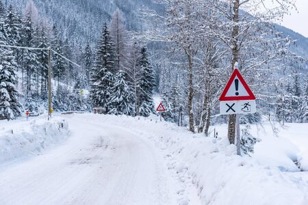 Red triangle road traffic warning sign - Other Danger. Crossroads with cross-country skis paths. Snow covered road, trees and mountains. Ski resort Schladming Dachstein, Austria.の写真素材