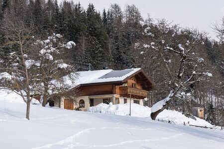 Solar photovoltaic panels PV on a snowy house roof. Electricity from the sun during winter. House in the mountains with snow covered trees at the background.の写真素材