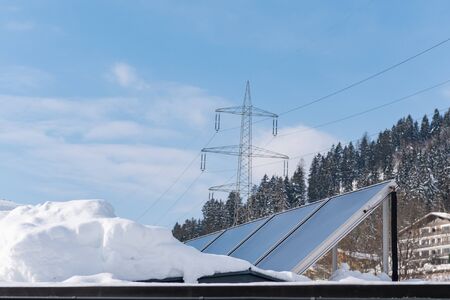 Photovoltaic panels partly covered with snow, installed on the roof of the house. In the background...