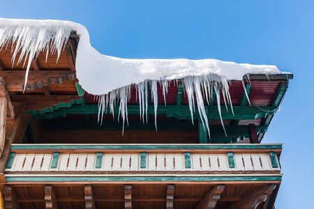 Big icicles hanging over the rain gutter on a roof of a traditional wooden house in the mountains in winter could be dangerous.の写真素材