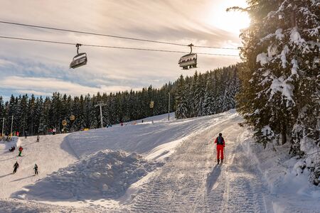 Skiers on a chair lift against the backdrop of the sun and trees, contour photo, orange shades, ski...