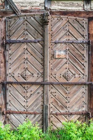 Old wooden door decorated with carved wood made flowers with corroded and rusty fittings and hinges. Details of wood and metal structure and green grass below.の写真素材