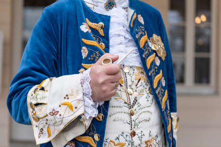 The details of man dressed in a baroque costume. A hand holding a pipe, golden buttons, vest and decorative hems.の写真素材