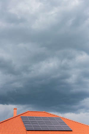 Red tile roof with photovoltaic panels during stormy weather. Solar PV installation and dark blue threatening sky in the background and copy space.の写真素材