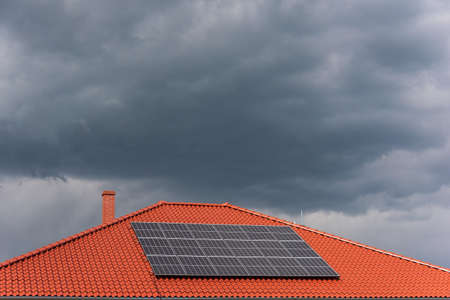 Red tile roof with photovoltaic panels during stormy weather. Solar PV installation and dark blue threatening sky in the background and copy space.の写真素材