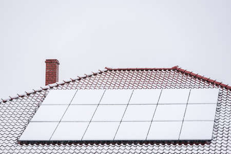Completely snow-covered house roof with photovoltaic solar panels in winter. Electricity from the sun during winter.の写真素材