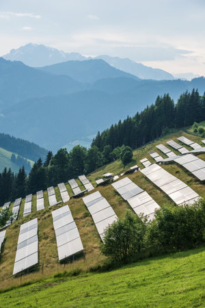 Photovoltaic farm located on a mountain slope in the Alps. Green pasture grass and blue skies and...