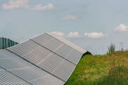 Solar, photovoltaic power station located on the hill. Green pasture grass and blue skies and white...