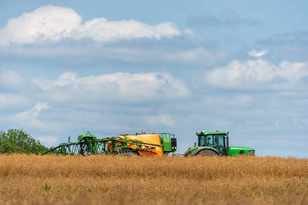 Agricultural tractor with sprayer spraying pesticides on the field in summer.