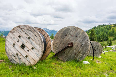 Large wooden cable pulleys with electric cables. Cable reels, cable drums lying on the construction site. In the background, the blue sky and mountains covered with green vegetationの写真素材