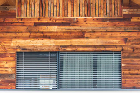 The faÃ§ade of the building with a large window with an external roller shutter, shutters and a wall faÃ§ade made of brown boardsの写真素材