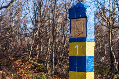Ukrainian blue and yellow number one border pillar with coat of arms. In the background, the blue...