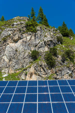 Solar photovoltaic panels against the backdrop of rocky mountains covered with green plants and treesの写真素材