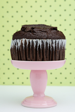 a chocolate muffin on a pink dessert stand pedestal against a  fun background in a dessert shop.の写真素材