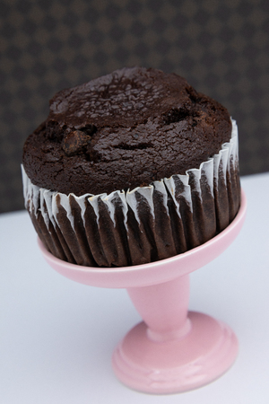 a chocolate muffin on a pink dessert stand pedestal against a  fun background in a dessert shop.の写真素材