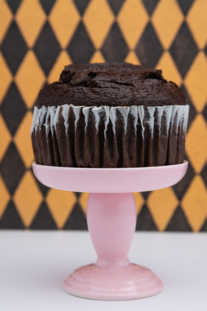 a chocolate muffin on a pink dessert stand pedestal against a  fun background in a dessert shop.の写真素材