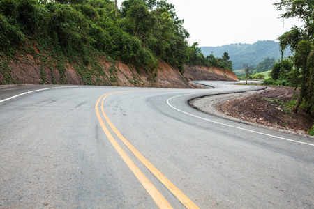 A rural mountain road with a winding "S" curve. The road fades into darker tones as it moves away from the viewer./in Thailand.の写真素材