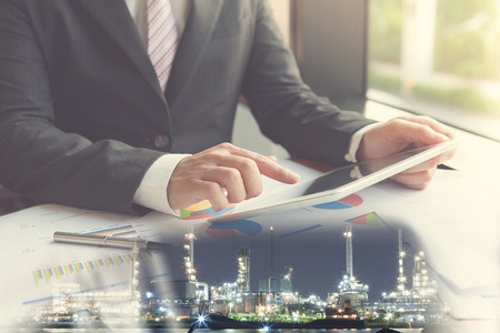 Double exposure businessman using the tablet in office with refinery and financial graph on blurred oil refinery background, Business Trading concept.の写真素材