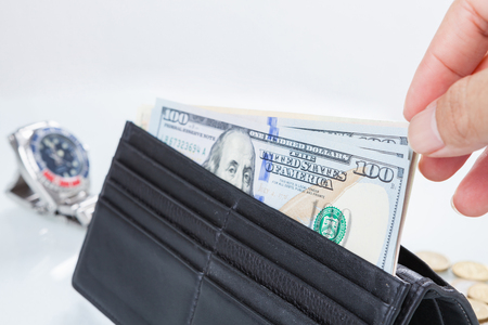 Buying time / hand holding wallet with dollar banknote trying to buy a clock.の写真素材