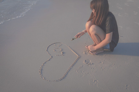 woman drawing a heart in the sand on a tropical beachの写真素材
