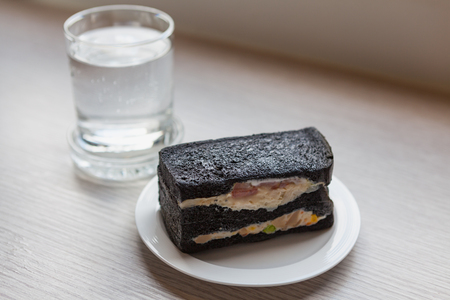 Charcoal sandwiches with Oclock and a glass of dringking water in morning time on wooden table in working roomの写真素材