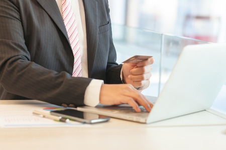 Businessman doing online banking, making a payment or purchasing goods on the internet entering his credit card details on a laptop, close up view of his handsの写真素材