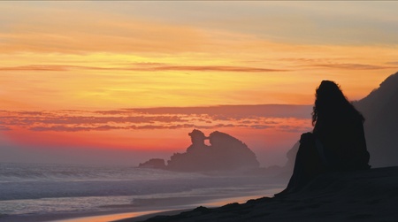 A girl observing the wonderful sunset in a beach の写真素材